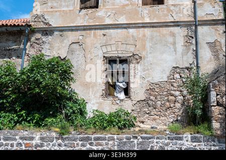 Altes offenes Fenster in einer alten Ruine mit Vorhängen und grünen Pflanzen an der zerbrochenen Wand. Stockfoto