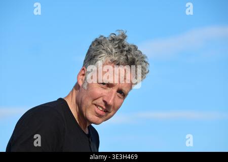 Porträt eines Mannes mittleren Alters im Freien mit einem klaren blauen Himmel im Hintergrund. Natürliches Licht, ehrlicher Ausdruck und moderner Lebensstil Stockfoto