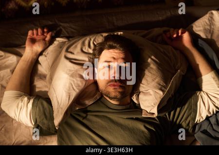 Porträt eines jungen Mannes, der wach im Bett liegt und nach oben starrt Stockfoto