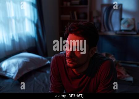 Junger Mann, der allein im Schlafzimmer sitzt und über das Leben nachdenkt Stockfoto