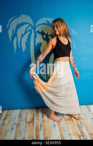 Frau mit Dreadlocks und Tätowierungen, die sich gegen eine blaue Wand mit Palmenschatten posiert Stockfoto