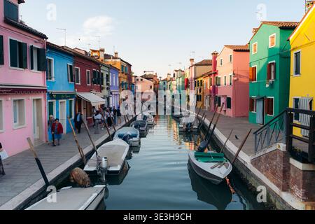 Der Blick auf die lebendigen Häuser reflektiert das stille Kanalwasser, in dem die Boote ankern, eine malerische Szene in Burano, Venedig, Italien. Stockfoto
