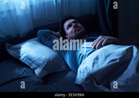 Erwachsener Mann, der nachts wach im Bett liegt und Smartphone hält Stockfoto