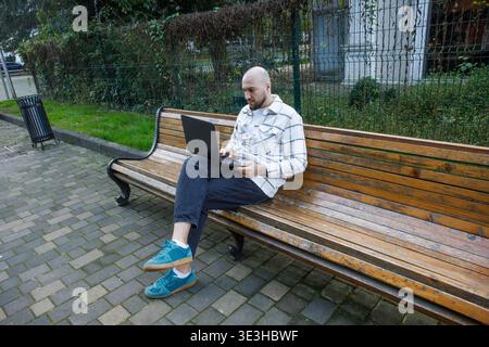 Kahler und bärtiger Mann, der draußen mit Laptop arbeitet Stockfoto