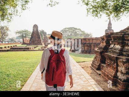 Junge Touristin in Strohhut und weißer Kleidung Spaziergang mit leichtem Stadtrucksack durch Ayutthaya Wat Phra RAM Alte Ruinen Straßen in Thailan Stockfoto