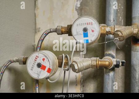 Detaillierte Nahaufnahme von zwei Wasserdurchflussmessern und zugehörigen Kupferrohranschlüssen an der Wand Stockfoto