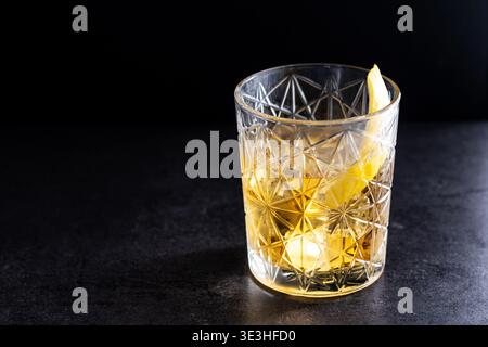 Rostiger Nagelcocktail mit Zitronenschale in Kristallglas auf schwarzem Schieferhintergrund Stockfoto