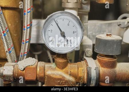 Nahaufnahme eines Manometermessstabes in industrieller Umgebung mit Rohrleitungen und Ventilen Stockfoto