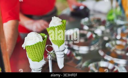 Eisverkäufer, der erfrischende Vanillekugeln in grünen Waffelkegeln serviert Stockfoto