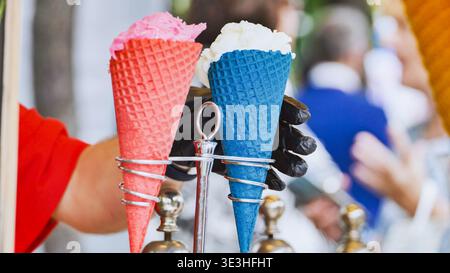 Anbieter, der zwei süße Eissorten in roten und blauen Kegeln hält und leckeres Dessert anbietet Stockfoto