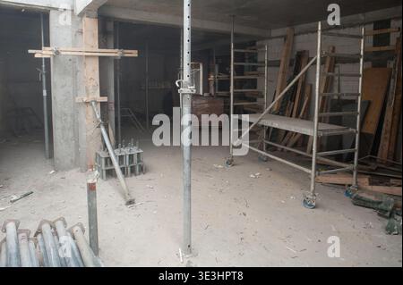 Innerhalb einer geräumigen Baustelle erheben sich Gerüsttürme, während die Arbeiter sorgfältig Rahmen und Balken für ein neues Gebäude errichteten. Staub wirbelt im A Stockfoto