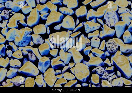 Kieselhintergrund mit einer Mischung aus fluoreszierenden blauen und gelben Steinen, die eine strukturierte Oberfläche mit verschiedenen Formen und Größen, ideal für Stockfoto