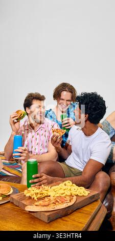 Eine Gruppe von Freunden genießt Fast Food und Getränke, die zusammen auf der Couch sitzen. Stockfoto