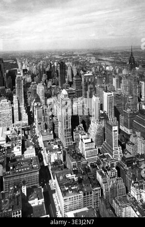 Dieses atemberaubende Schwarzweiß-Luftbild erfasst einen atemberaubenden Blick auf die Stadt Midtown Manhattan in New York City, wahrscheinlich in den 1950er Jahren von Angelo Rizzuto aufgenommen. Der berühmte Chrysler Building Turm und zahlreiche Hochhäuser dominieren den Horizont und zeigen die architektonische Pracht des alten New Yorks. Das Bild bietet einen Einblick in die städtische Entwicklung und ein Gefühl des täglichen Lebens in der geschäftigen Metropole jener Zeit. Stockfoto