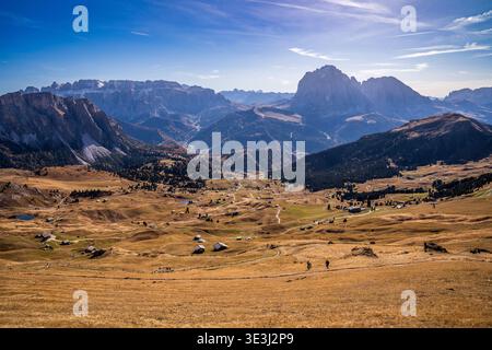 Panoramablick auf die Dolomiten von Seceda aus. Goldene Wiesen mit Holzhütten, Wanderer auf Wanderwegen und die majestätischen Gipfel des Langkofs und der Sella Stockfoto