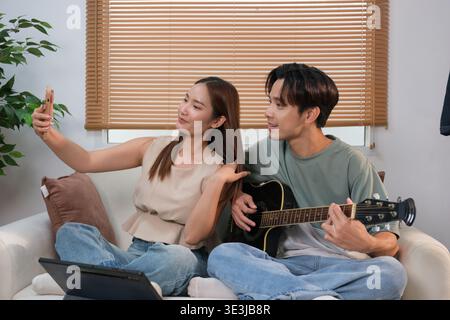 Ein junges asiatisches Paar verbringt seine Freizeit mit Gitarre und Gesang zu Hause. Stockfoto
