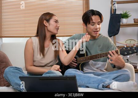 Ein junges asiatisches Paar verbringt seine Freizeit mit Gitarre und Gesang zu Hause. Stockfoto