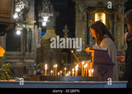 Santa Maria in Aracoeli Basilika (Basilica di Santa Maria in Aracoeli), Rom, Italien. Frau zündet Votivkerzen in dunklem Inneren an, religiöse Hingabe Stockfoto