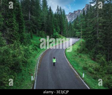 Frau, die auf einer gewundenen Straße in üppig grünen Wäldern läuft. Antenne Stockfoto