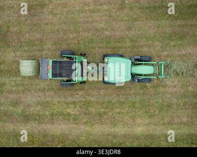 Cumberland, Maine – ein grüner Traktor, der eine Rundballenpresse über ein trockenes Heufeld zieht und während der Ernte zylindrische Heuballen bildet Stockfoto