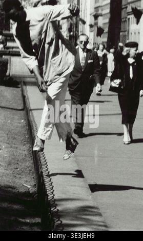 Dieses eindrucksvolle Straßenfoto wurde in den 1940er Jahren von Angelo Rizzuto aufgenommen und zeigt einen jungen Mann, der dynamisch über einen niedrigen Zaun oder Bordstein in New York City springt. Das Bild zeigt Mode und Alltag aus der Mitte des Jahrhunderts, mit Fußgängern im Hintergrund, die das geschäftige Stadtbild verstärken. Rizzutos Arbeit konzentrierte sich oft auf ehrliche Momente innerhalb der Stadt. Stockfoto
