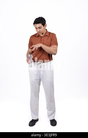 Junger Mann, der Wasser aus einer Flasche in ein Glas im Studio gießt Stockfoto