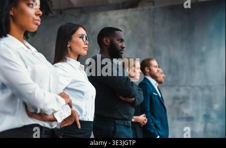 Gruppe von Personen, die bei einer formellen Veranstaltung am Arbeitsplatz in einer modernen Umgebung mit überkreuzten Armen stehen Stockfoto