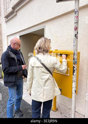Gelbe Sammelbox des Postamtes der Vatikanstadt. Touristen, die Briefe in der Nähe historischer Architektur in Vatikanstadt, Italien versenden. Stockfoto