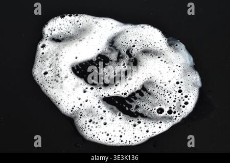 Eine Pfütze aus weißem Seifenschaum auf schwarzem Hintergrund. Stockfoto