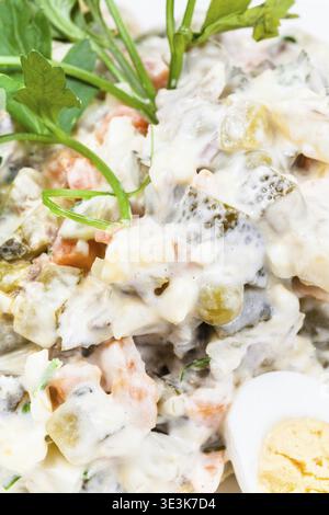 Russischer Salat mit Mayonnaise aus nächster Nähe, dekoriert mit Gemüse und gekochten Eiern Stockfoto