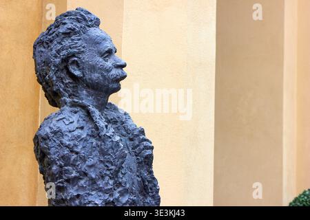 Eine Bronzestatue von Albert Einstein in Profilansicht vor einem beigefarbenen und gelb strukturierten Wandhintergrund. Die Skulptur zeigt einen Stockfoto