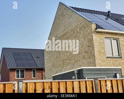 Nahaufnahme der modernen Wohnarchitektur mit zwei Häusern mit Photovoltaik-Solarpaneelen auf dunklen Ziegeldächern. Im Vordergrund Stockfoto