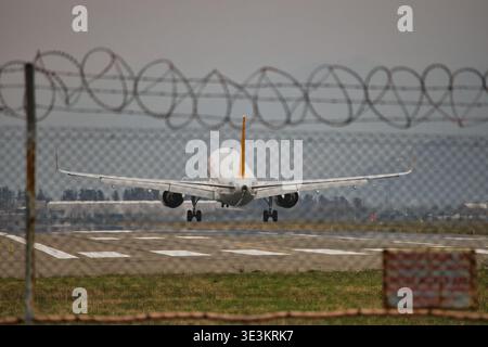 Eine professionelle Tele-Aufnahme eines kommerziellen Jet, der auf einer Start- und Landebahn landet. Die Perspektive wird hinter einem Maschendrahtzaun mit Ba erfasst Stockfoto