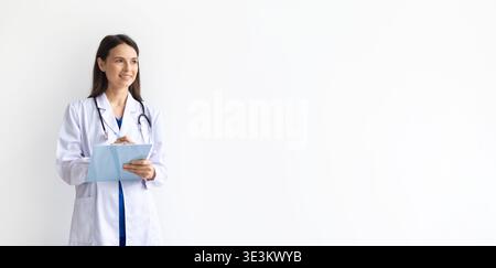 Ärztin, die einen medizinischen Mantel trägt und die Zwischenablage hält und auf den Kopierraum blickt Stockfoto