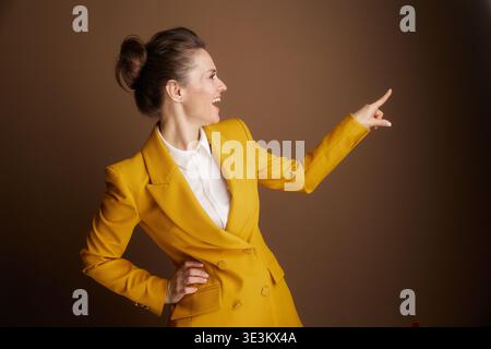Eine lächelnde Profi in einem gelben Blazer zeigt selbstbewusst nach rechts mit der Hand auf der Hüfte, lenkt die Aufmerksamkeit oder zeigt einen klaren Weg in einem an Stockfoto
