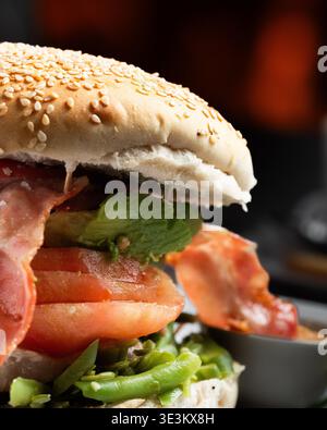 Sesambrötchen enthält saftiges, geschichtetes Fleisch und Gemüse. Leuchtend rote Tomaten blicken über knusprige grüne Bohnen. Knusprige Specklocken sorgen für herzhaften Kontrast Stockfoto