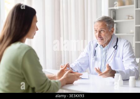 Leitender männlicher Arzt im Gespräch mit weiblicher Patientin während ärztlicher Beratung in der Klinik Stockfoto