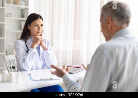 Ärztin, die während der Sprechstunde in der Klinik sorgfältig auf ältere männliche Patienten hört Stockfoto