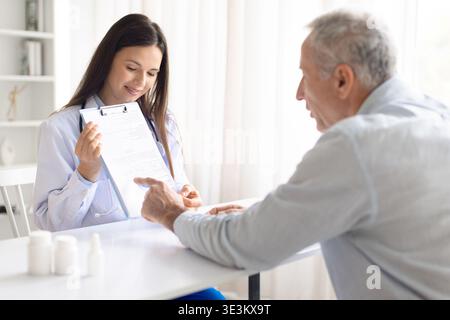 Ärztin, die mit Seniorpatienten in der Klinik ein medizinisches Dokument überprüft Stockfoto