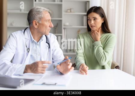Weibliche Patientin berührt den Hals und erklärt dem Arzt in der Klinik Symptome Stockfoto