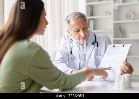 Leitender männlicher Arzt, der der Patientin medizinische Unterlagen und Behandlungsplan erklärt Stockfoto