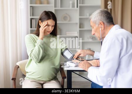 Schwangere Frau leidet unter Schwindel, während der Arzt während der pränatalen Beratung den Blutdruck kontrolliert Stockfoto