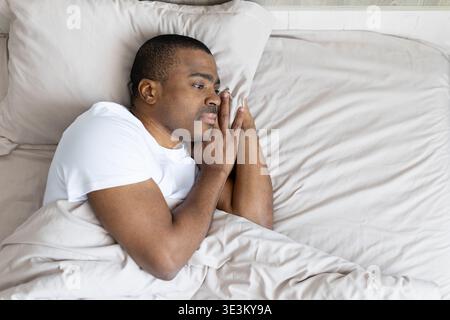 Junger schwarzer Mann, der im Bett liegt und nachdenklich und wach aussieht Stockfoto