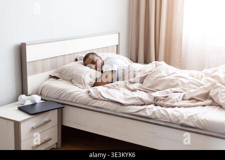 Junger schwarzer Mann, der friedlich im Bett schläft und bequem im Schlafzimmer ruht Stockfoto