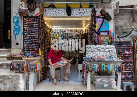 Ein türkischer Ladenbesitzer liest vor einem farbenfrohen Souvenir- und Juweliergeschäft in Istanbul, Türkei, die von Schmuckstücken und Accessoires umgeben ist Stockfoto