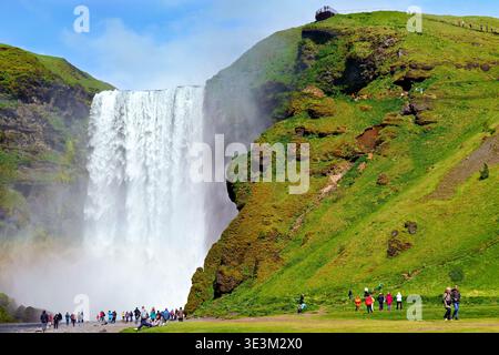 Besucher treffen sich in der Nähe des Wasserfalls Skogafoss in Island, genießen die Aussicht und machen Fotos an einem sonnigen Tag im Sommer. Stockfoto