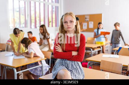 Trauriges langweiliges Mädchen, das getrennt im Klassenzimmer sitzt, in der Pause zwischen den Unterrichtsstunden Stockfoto