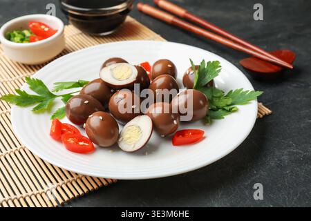 Eingelegte Wachteleier und Zutaten auf schwarzem Tisch, Nahaufnahme Stockfoto