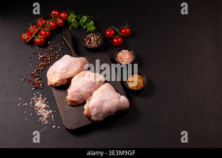 Rohe Hähnchenschenkel auf einem hölzernen Schneidebrett mit Kirschtomaten, Sellerie, gemischten Pfefferkörnern, himalaya-Salz und Vollkornsenf in kleinen Schüsseln, Stockfoto