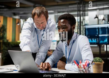 Geschäftsmann berät afroamerikanische Mitarbeiter bei der erfolgreichen Planung von Investitionsprojekten. Verschiedene männliche Büromitarbeiter analysieren Berichte und Geschäftslösungen im professionellen Arbeitsumfeld. Stockfoto